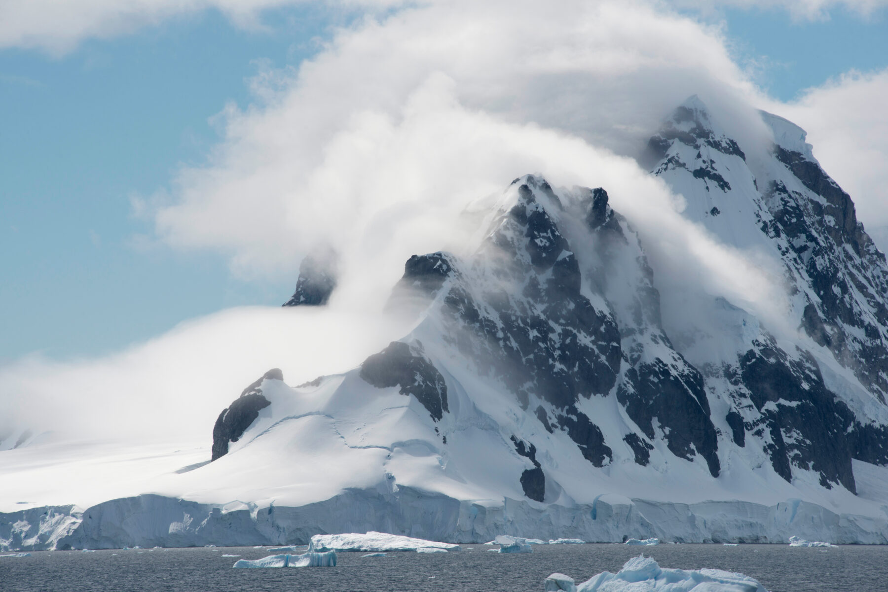 Antarctic Coastline With Snow Capped Mountains And Low Clouds