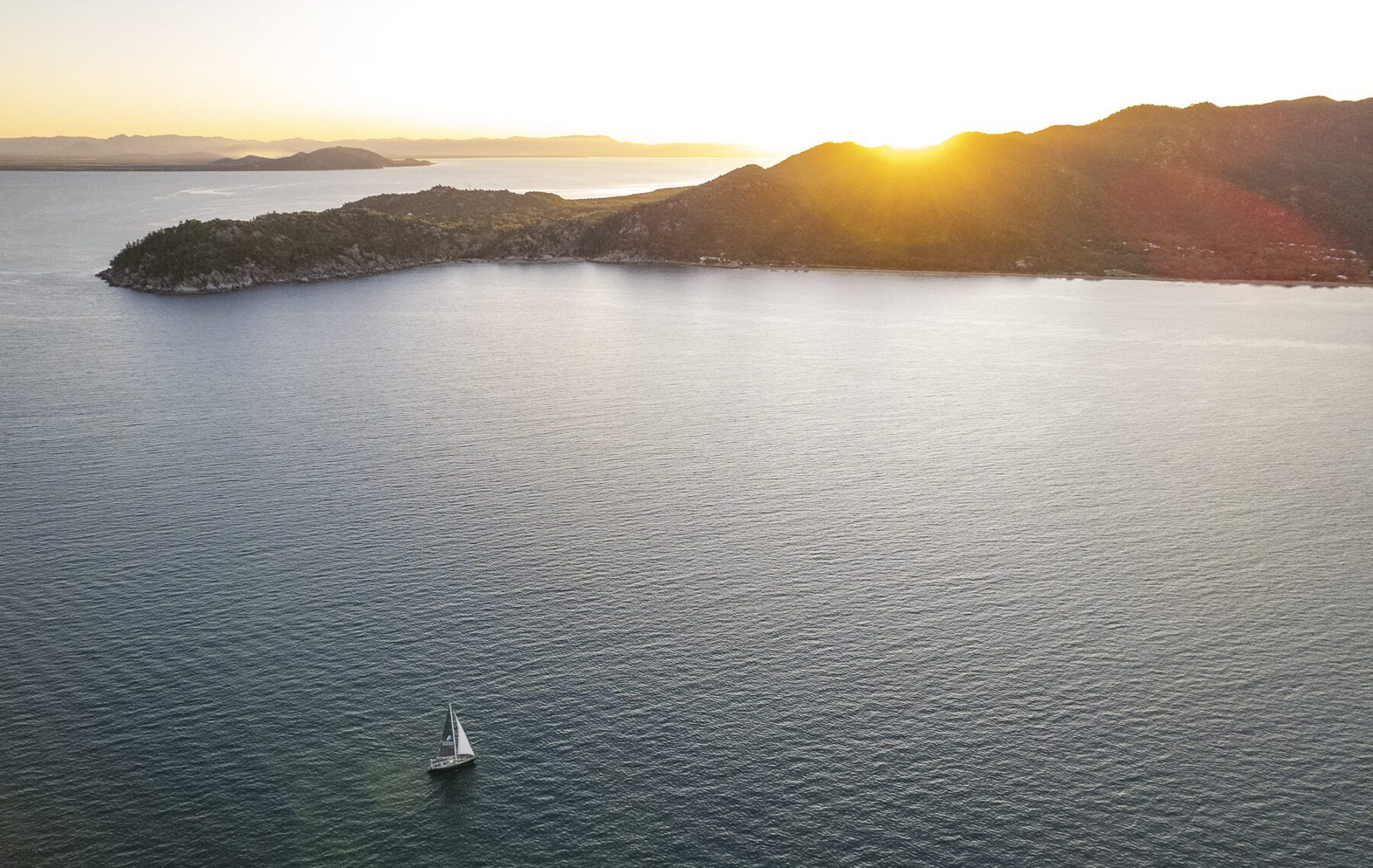 An aerial view of an Magnetic Island sunset with a yacht sailing in front of it